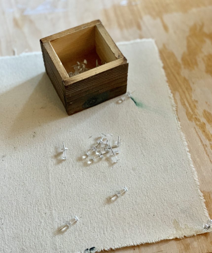 A box of push pins sitting on a piece of un-primed canvas