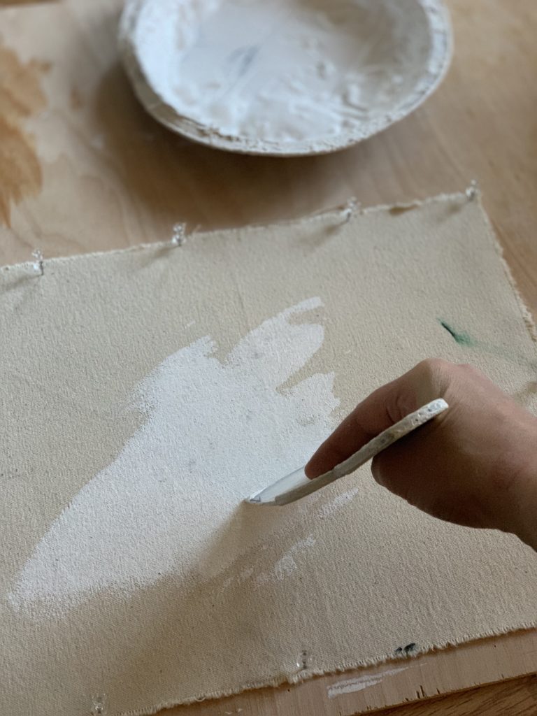 Artists hand holding a tool gesso priming a piece of canvas