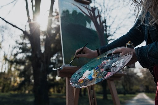 a woman holding a palette and brush working on a landscape oil painting for beginners outdoors 