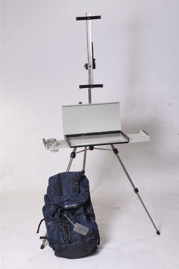 tripod easel with palette box tray pictured in a white room and a blue travel case resting on the floor