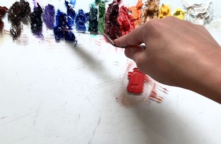 Artist with palette knife mixing cool red colors on a glass palette