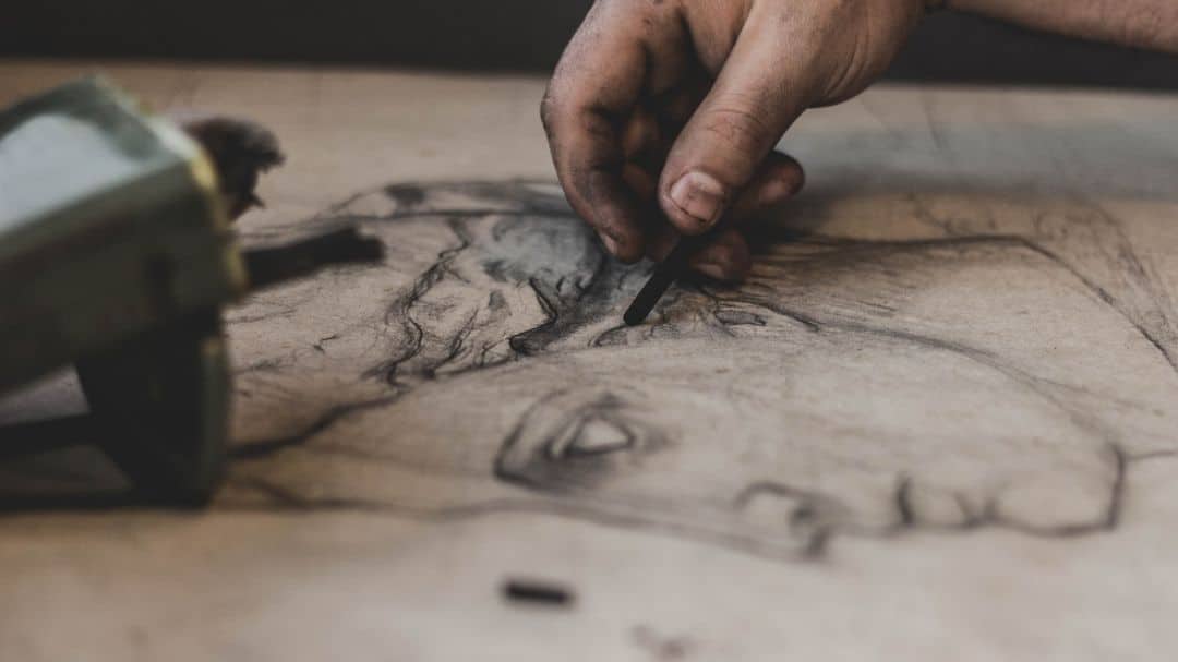 artist's hand holding charcoal working on drawing ideas on paper